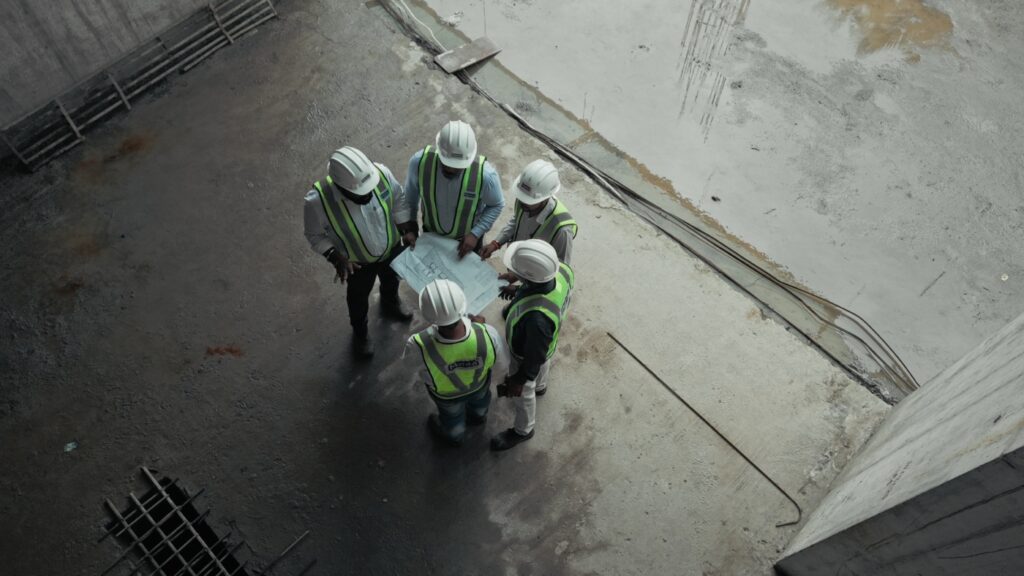 A professional team of engineers and architects from the Mehta Group collaborating over a technical blueprint at a construction site, demonstrating precision planning and expert project management in real estate development.